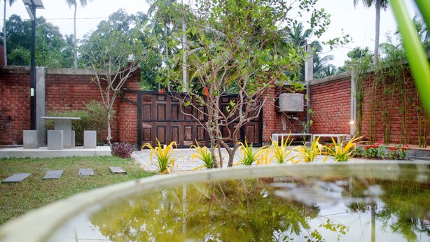 A courtyard with a pond, brick walls, and a wooden gate. - Laana Villa (Negombo)