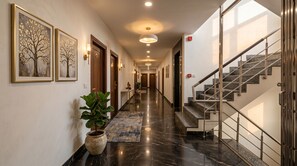 A hotel hallway with a marble floor, a staircase, and framed artwork on the walls.