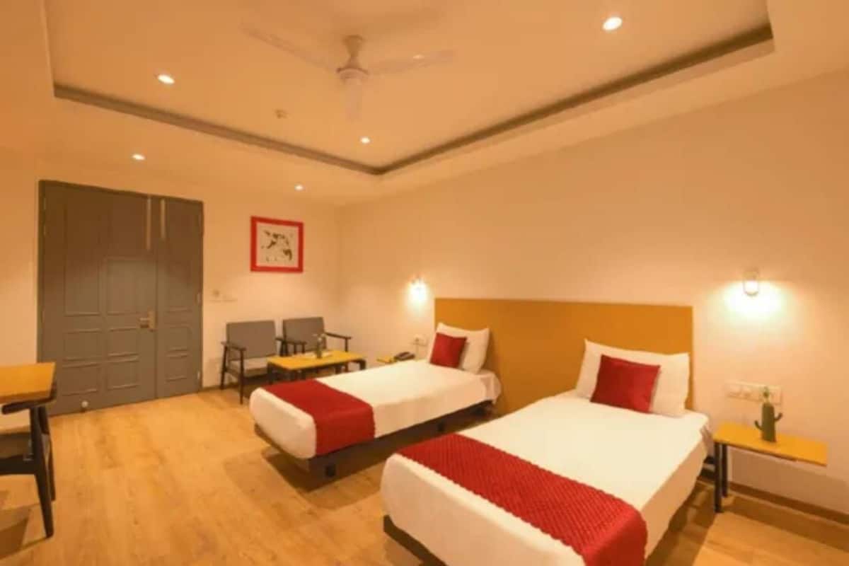 Une chambre d’hôtel avec deux lits, un bureau, une chaise, une armoire et un ventilateur de plafond.