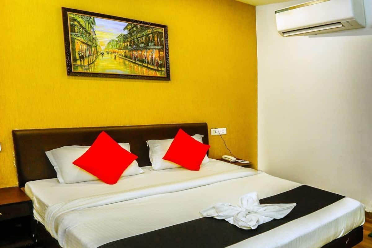 Une chambre d’hôtel avec un lit, un tableau au mur, un appareil de climatisation et un plancher en bois.