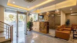 A reception area with a glass partition, a reception desk, a digital clock, and a seating area with sofas.
