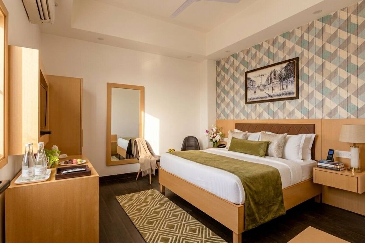 Une chambre d’hôtel comprenant un lit, une table de chevet, une commode, un bureau, une chaise, un miroir et un mur décoré d’un motif.