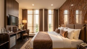 A hotel room with a bed, desk, TV, and a view of the outdoors.