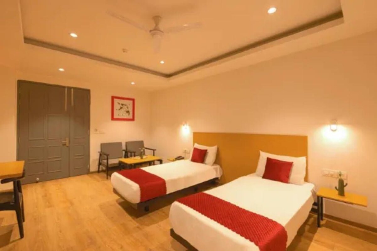 A hotel room with two beds, a desk, a chair, a wardrobe, and a ceiling fan.