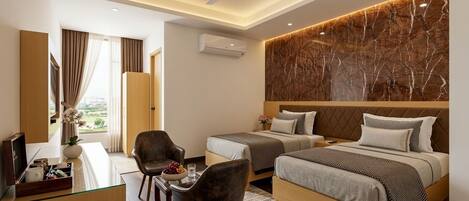 A hotel room with two beds, a desk with a chair, a TV, and a large window with curtains.