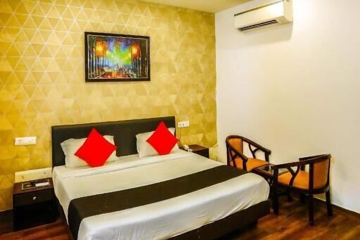 Une chambre d’hôtel avec un lit, une chaise, un tableau au mur et un appareil de climatisation.