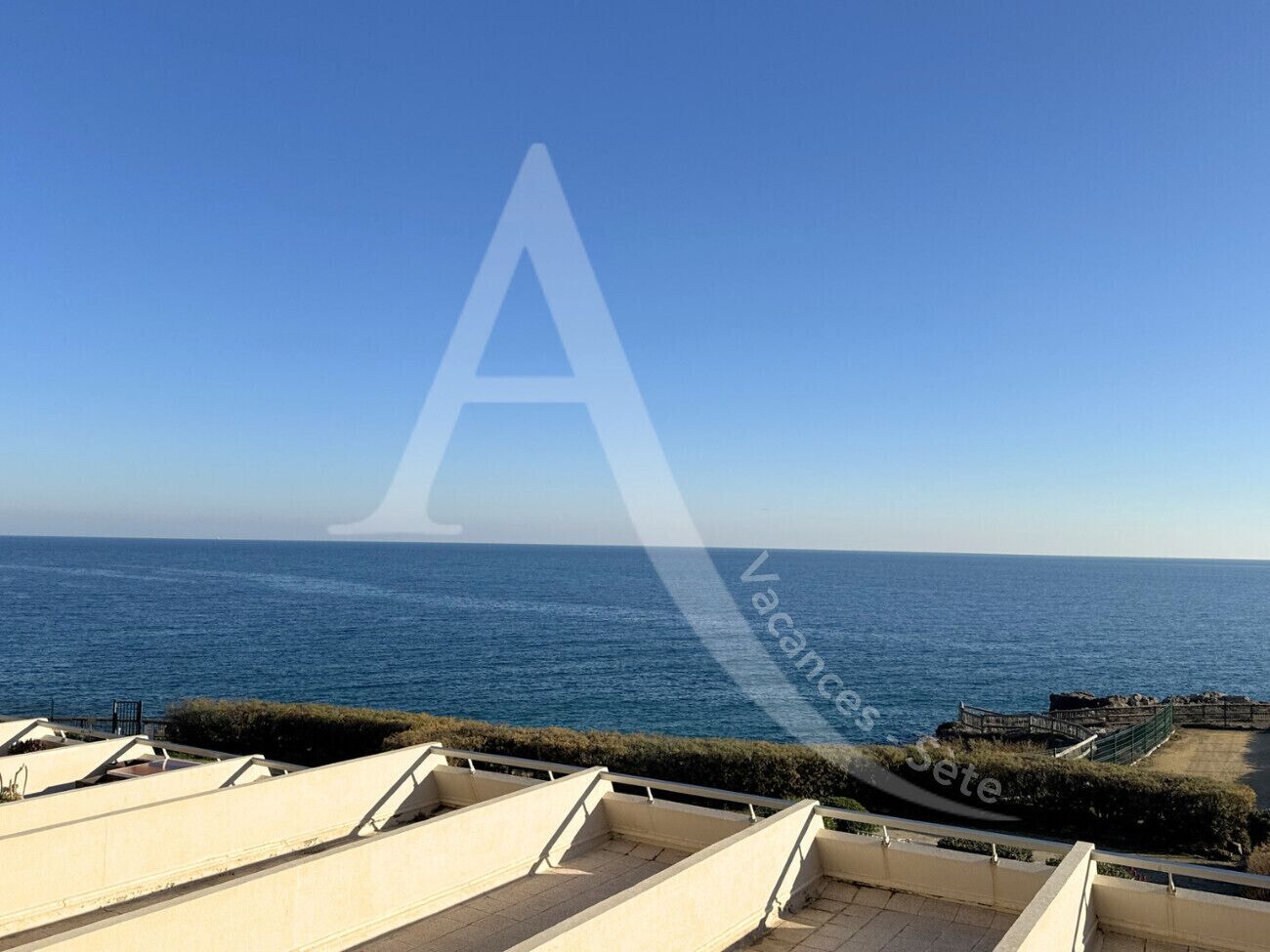 Vista sulla costa con cielo sereno, mare e area pavimentata con recinzione.
