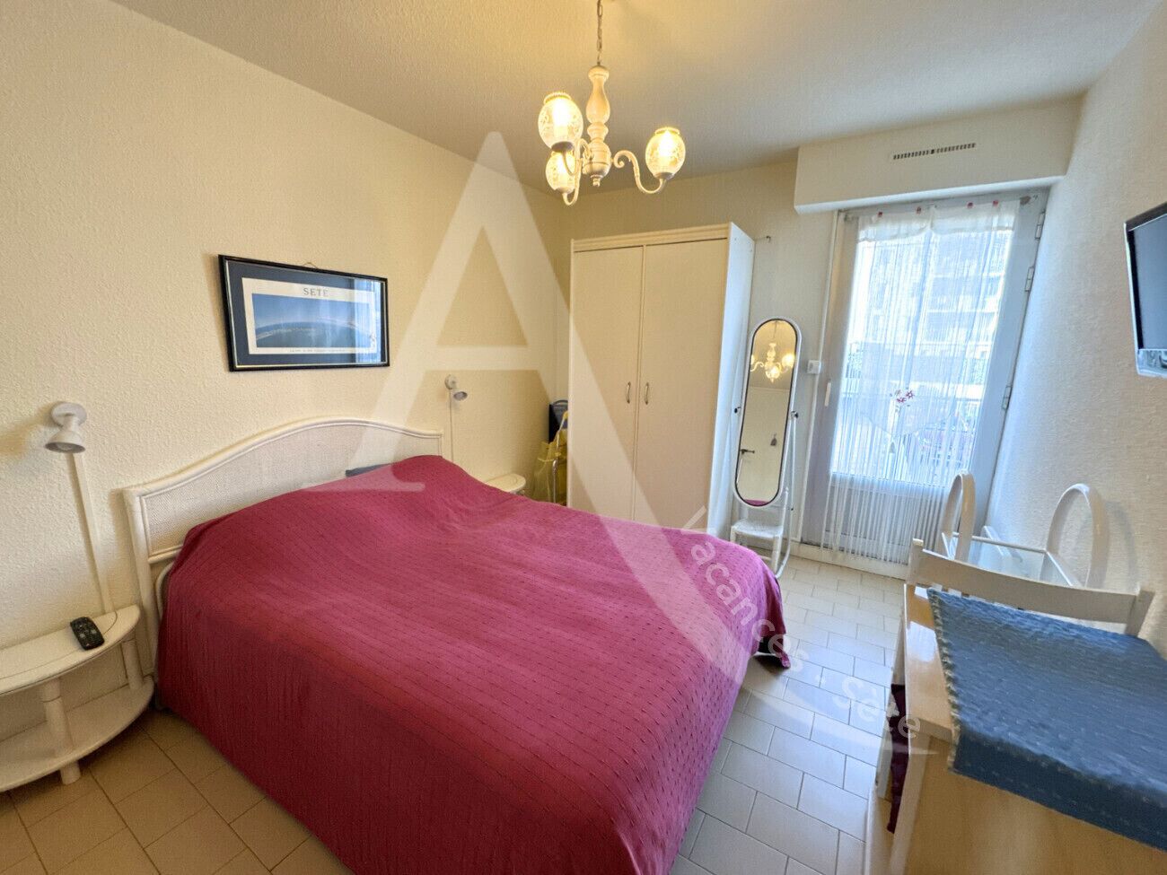 A bedroom with a bed, bedside table, lamp, wardrobe, and a window with curtains.