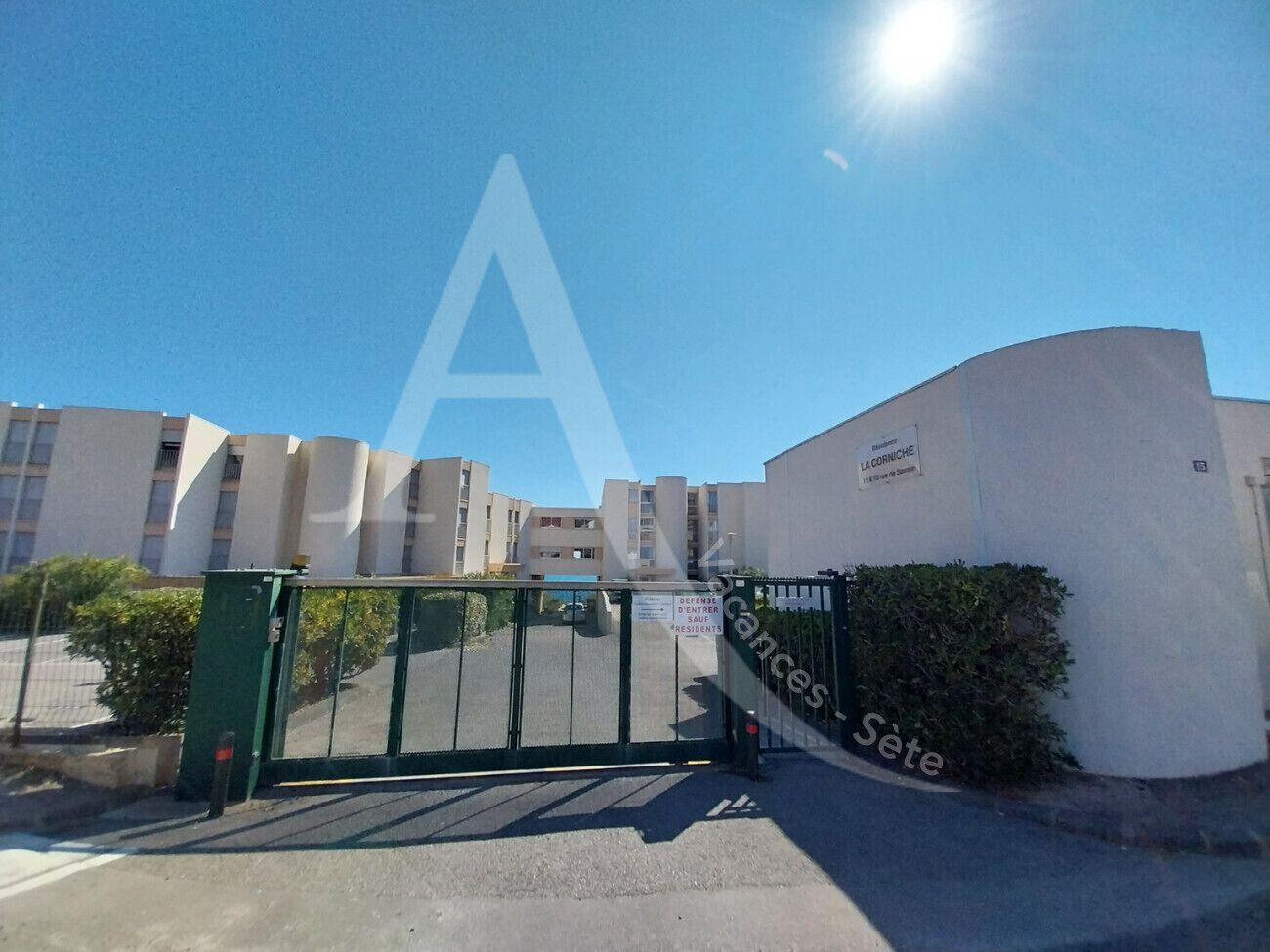 A gated entrance to a residential building complex with multiple apartment buildings in the background.