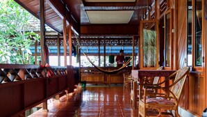 A covered corridor with wooden flooring and benches, leading to a seating area with tables and chairs. - Panorama Backpackers (Pulau Bunaken)