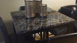 A dining area with a marble table, three textured candle holders, and a large abstract painting on the wall.