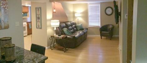 A living room with a sofa, a dining table with chairs, a lamp, and a clock on the wall.