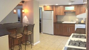 A kitchen with a gas stove, a refrigerator, and wooden cabinets. There are two bar stools and a countertop.