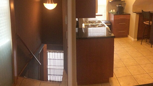 A kitchen with a gas stove, a coffee maker, and a bar stool.