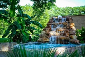 A stone waterfall feature with a pool in front, surrounded by lush greenery.