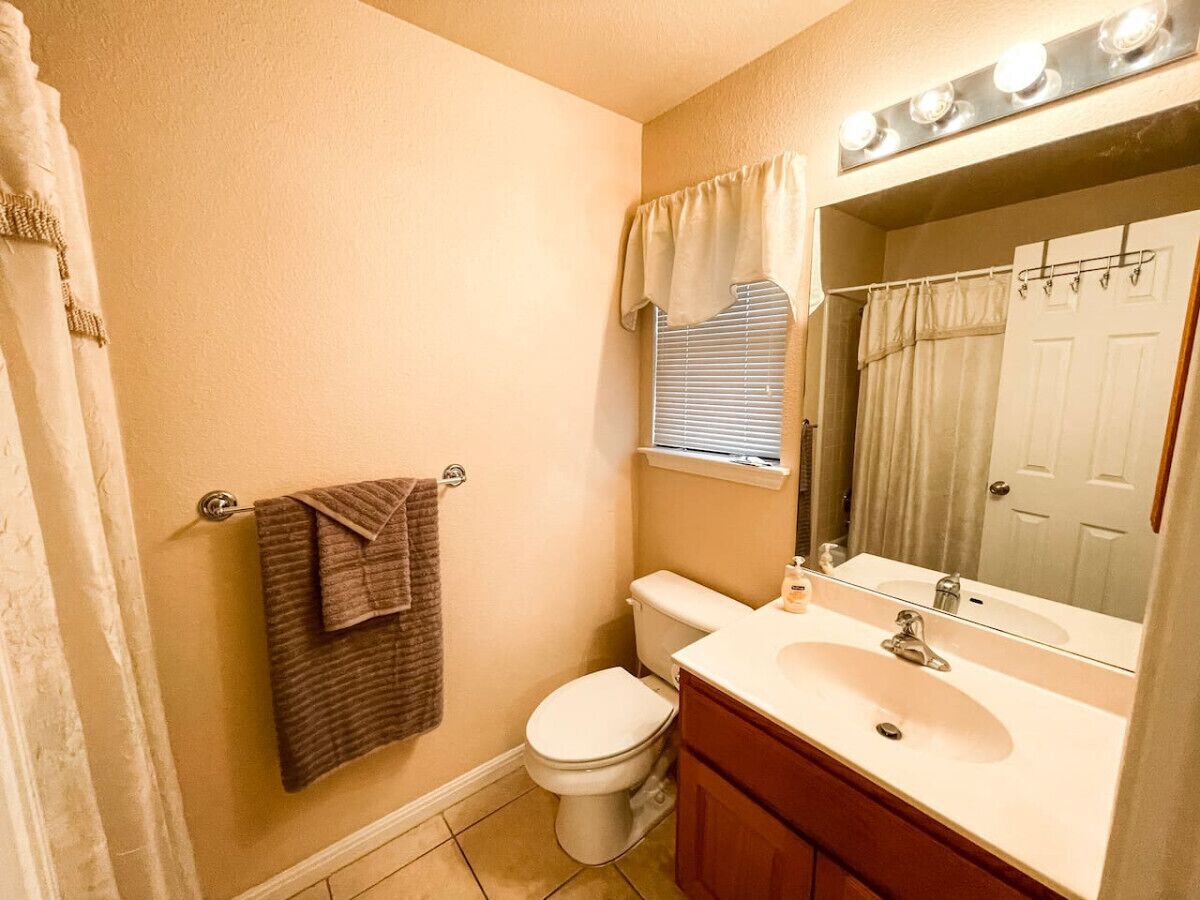 A bathroom with a toilet, sink, mirror, and towel rack.