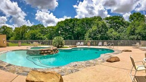 Una piscina con borde de piedra, sillas de descanso y un área cercada con árboles al fondo.
