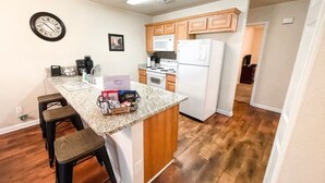 Una cocina con una isla central, armarios de madera, microondas, refrigerador y un reloj en la pared.