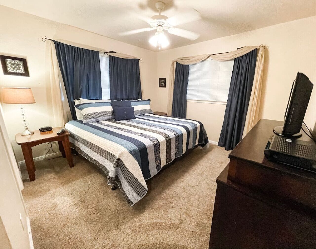 Un dormitorio con cama, escritorio con computadora, lámpara y cortinas.
