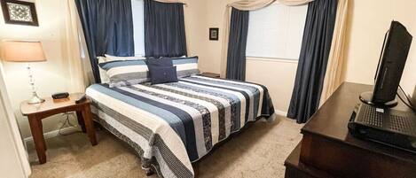 Un dormitorio con cama, escritorio con computadora, lámpara y cortinas.
