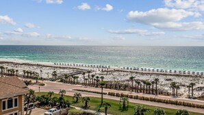 A beach with a paved walkway, palm trees, and a road in the foreground.