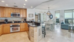 A modern kitchen with wooden cabinets, stainless steel appliances, and a large island. There is a dining area with a view of the ocean.