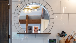 Une cuisine moderne avec des carreaux blancs, un banc en bois, un miroir rond et une horloge.