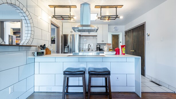 Une cuisine moderne dotée d’un îlot central, de deux tabourets, d’appareils électroménagers en acier inoxydable et de luminaires suspendus.