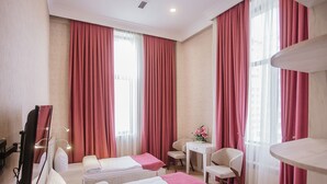 Una habitació d'hotel amb dos llits, una taula, una cadira i grans finestres amb cortines vermelles.