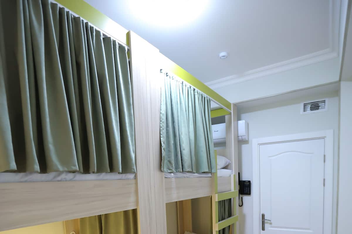 Une chambre avec un lit superposé, une porte blanche, une table de chevet et un téléphone fixé au mur.