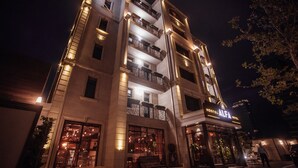 Un hotel amb diversos pisos, balcons, una entrada ben il·luminada i una placa ben visible que diu "ALFA HOTEL".