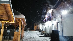 Ein verschneiter Außenbereich mit Holzbauten und Steinstufen, beleuchtet mit Lichterketten.
