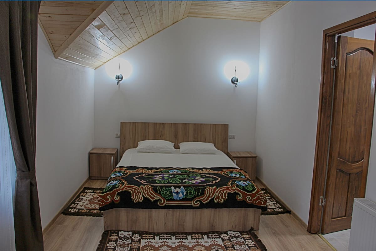 A bedroom with a wooden headboard, a patterned bedspread, two bedside tables, and a nightstand.
