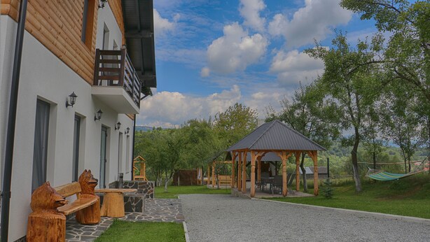 Ein Gebäude mit Holzfassade, eine Steinsitzbank, ein Gazebo und eine Rasenfläche.