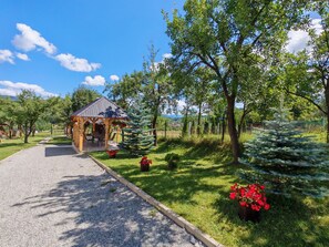 A wooden gazebo with a gravel path leading to it, surrounded by lush greenery and trees. - Pensiunea Maramures Landscape (Moisei)