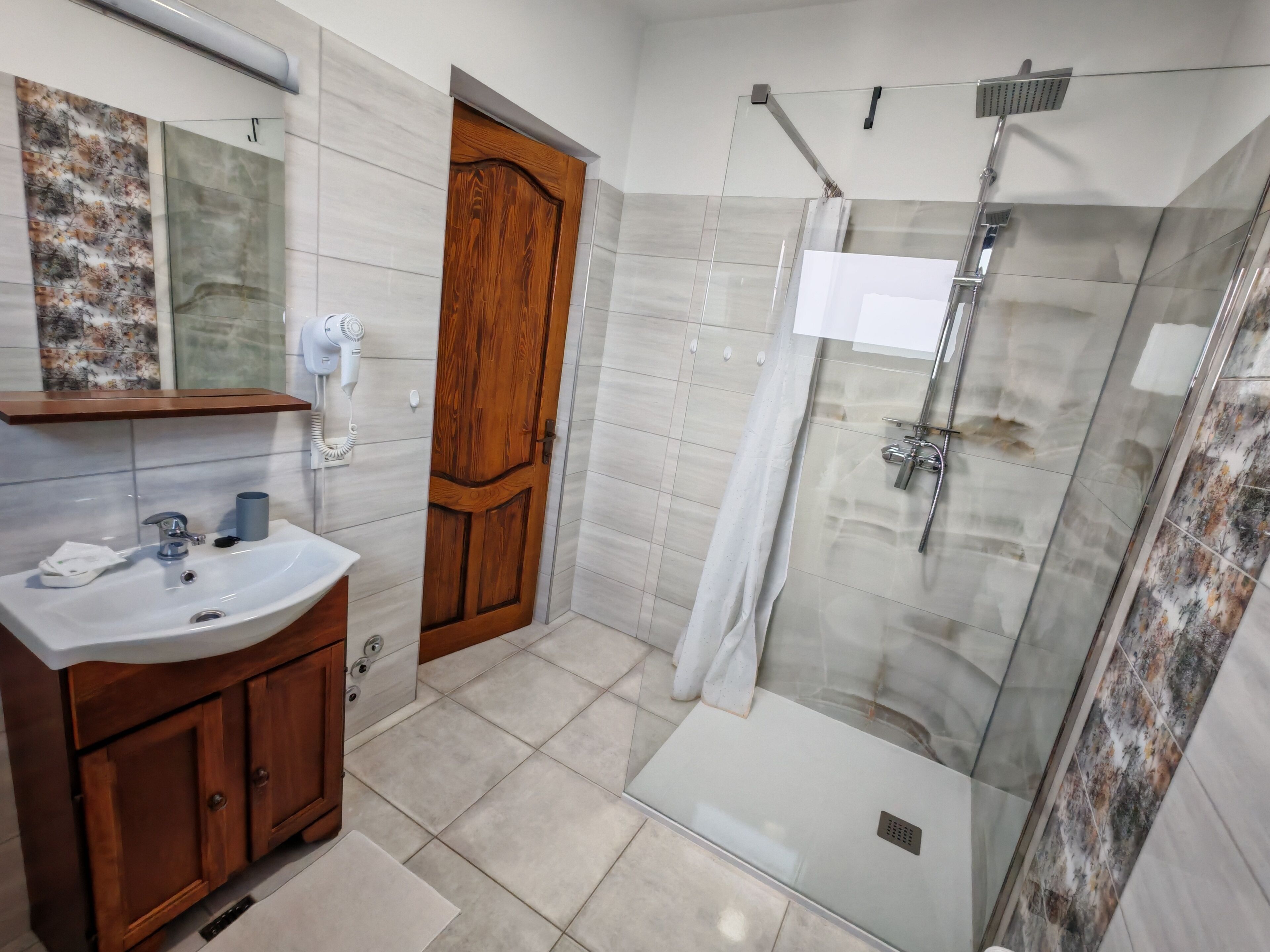 Une salle de bain avec une porte en bois, un lavabo avec un miroir et une douche séparée par des parois en verre.