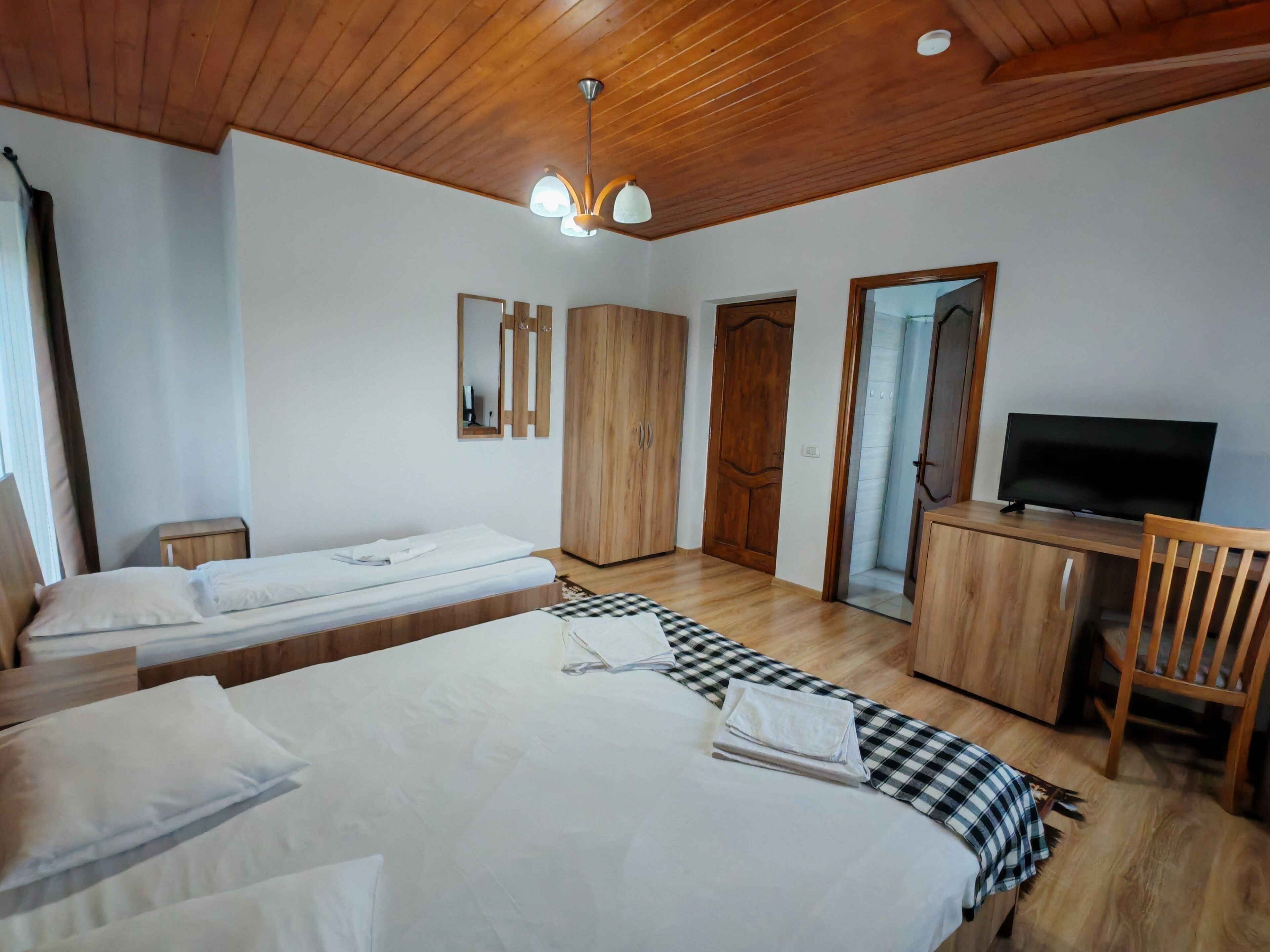 A hotel room with two beds, a desk with a TV, wooden wardrobe, and a mirror.