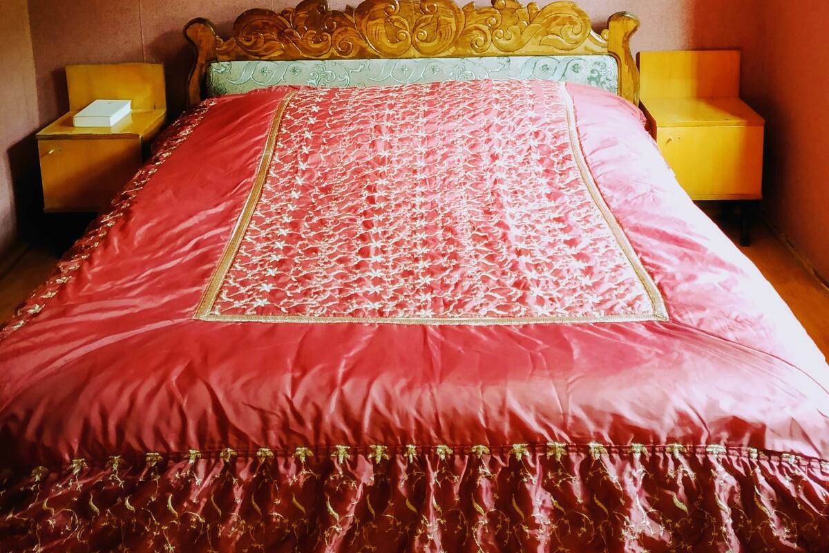 Una cama con una colcha roja y dorada, dos mesitas de noche y un cabecero con diseño floral.