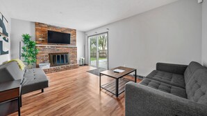 Ein modernes Wohnzimmer mit Kamin aus Backsteinen, einem Flachbildfernseher, einem grauen Sofa und einem Couchtisch.