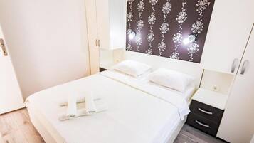 A neatly made bed with white linens, a dark patterned headboard, and a bedside table with a lamp.