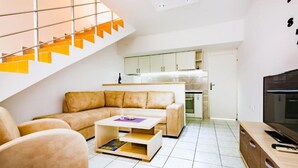 Ein modernes Wohnzimmer mit einer Couch, einem Couchtisch und einem Fernseher. Es gibt eine Küchenzeile mit Schränken und eine Treppe mit orangefarbenen Akzenten.