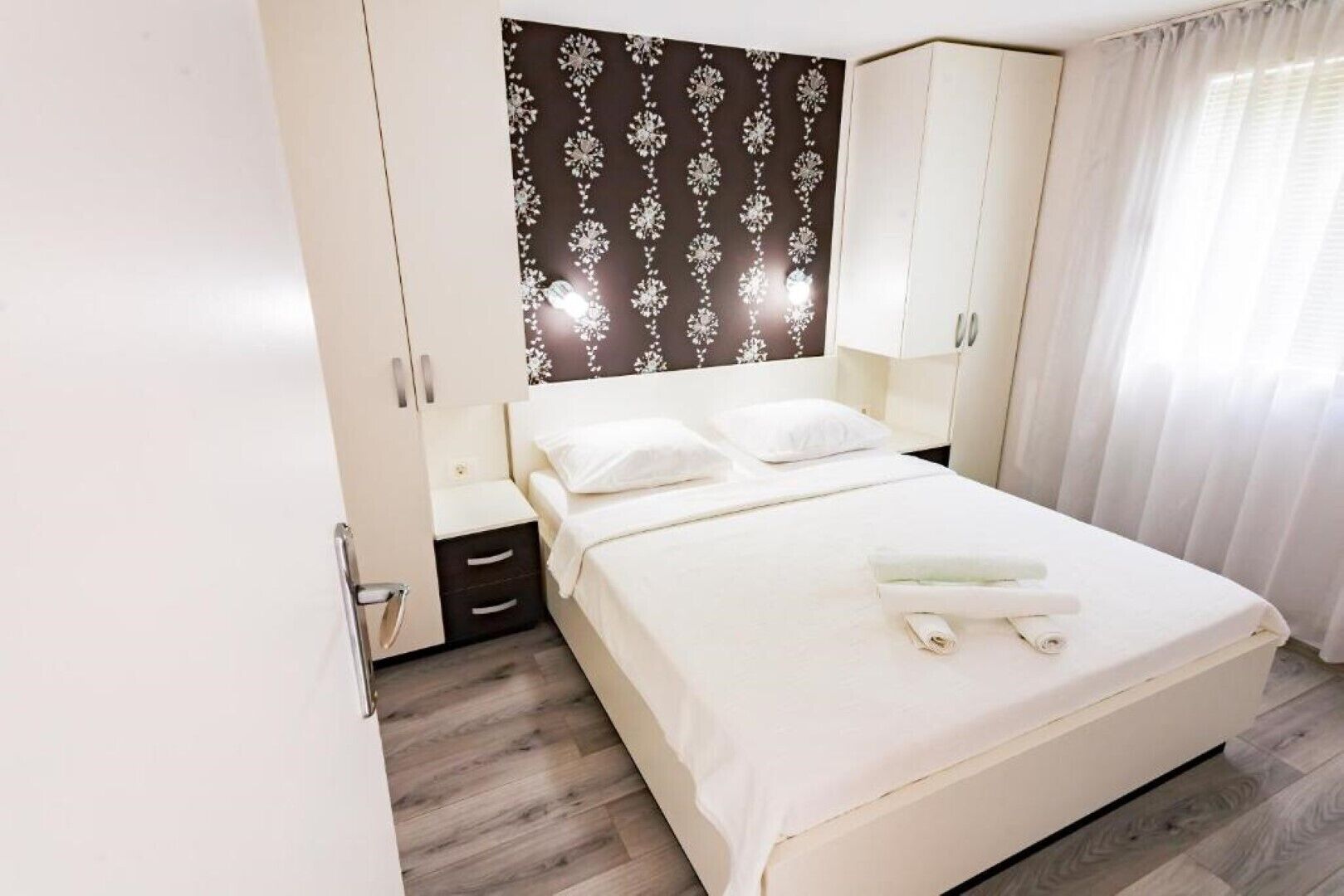 Een hotelkamer met een bed, nachtkastje, kledingkast en raam met gordijnen.