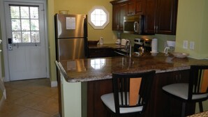 A kitchen with a stainless steel refrigerator, a microwave, a stove, and a sink. There are two bar stools and a window with blinds. - PLUNGE POOL VILLA ON BLUE WATER LAGOON DUCK Key/MARATHON, FL (Marathon)