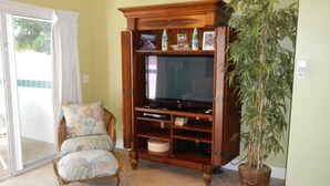 A living room with a wooden entertainment center, a wicker chair, and a large potted plant. - PLUNGE POOL VILLA ON BLUE WATER LAGOON DUCK Key/MARATHON, FL (Marathon)