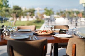 Una mesa de comedor dispuesta con platos, cubiertos y una pizza, con un letrero que dice 'Reserved', en un restaurante con terraza.
