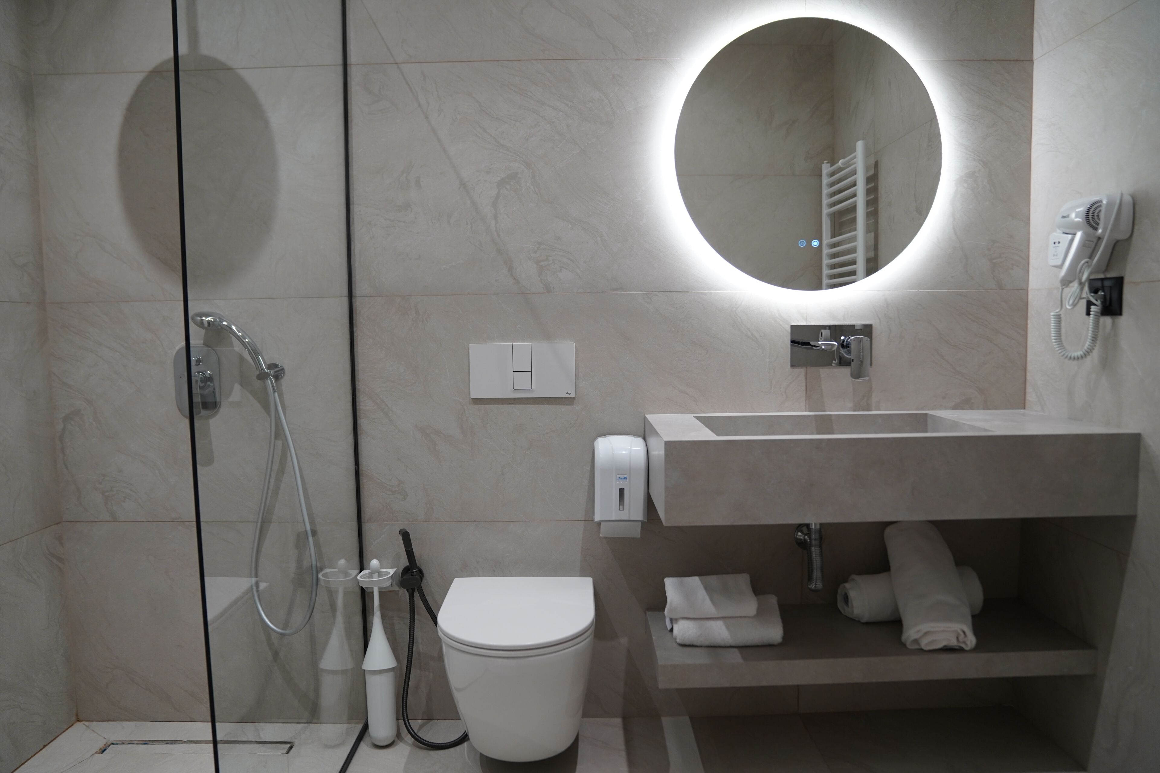 Une salle de bain moderne avec une douche à parois de verre, des toilettes, un lavabo avec un miroir et un porte-serviettes.