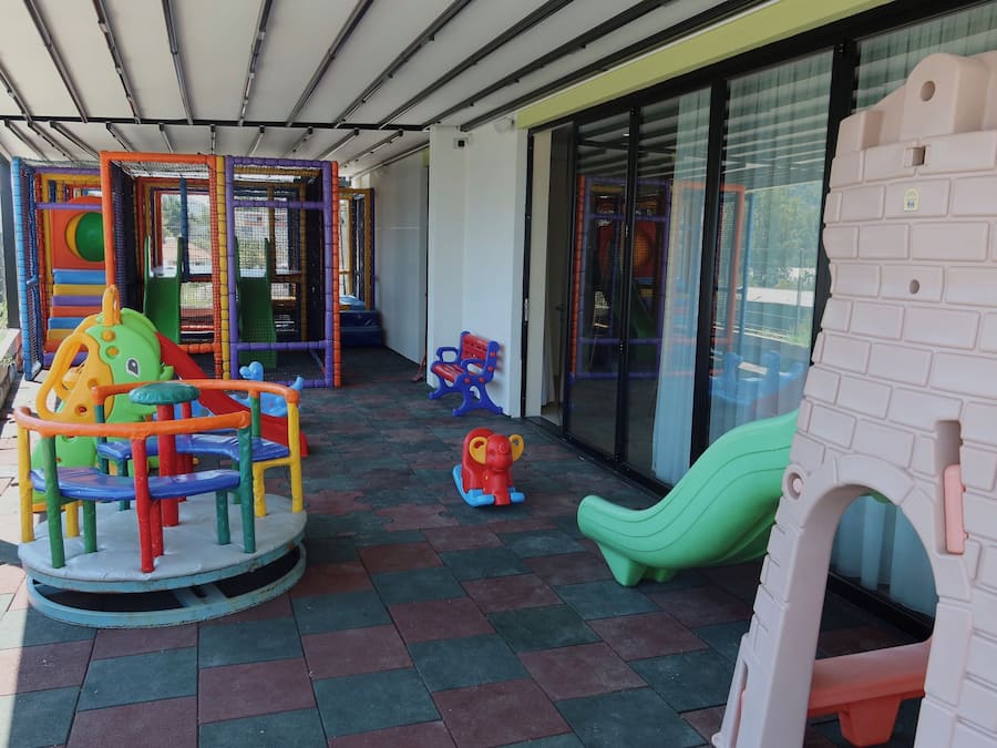 A covered outdoor play area with various play structures, including a climbing frame, a slide, and a small ball pit.
