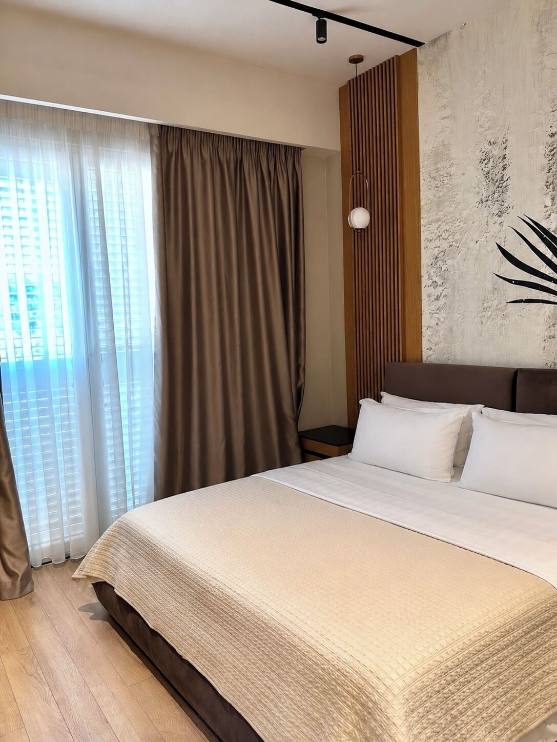 Habitación de hotel con una cama grande, vistas de la ciudad a través de la ventana y una pared con textura.