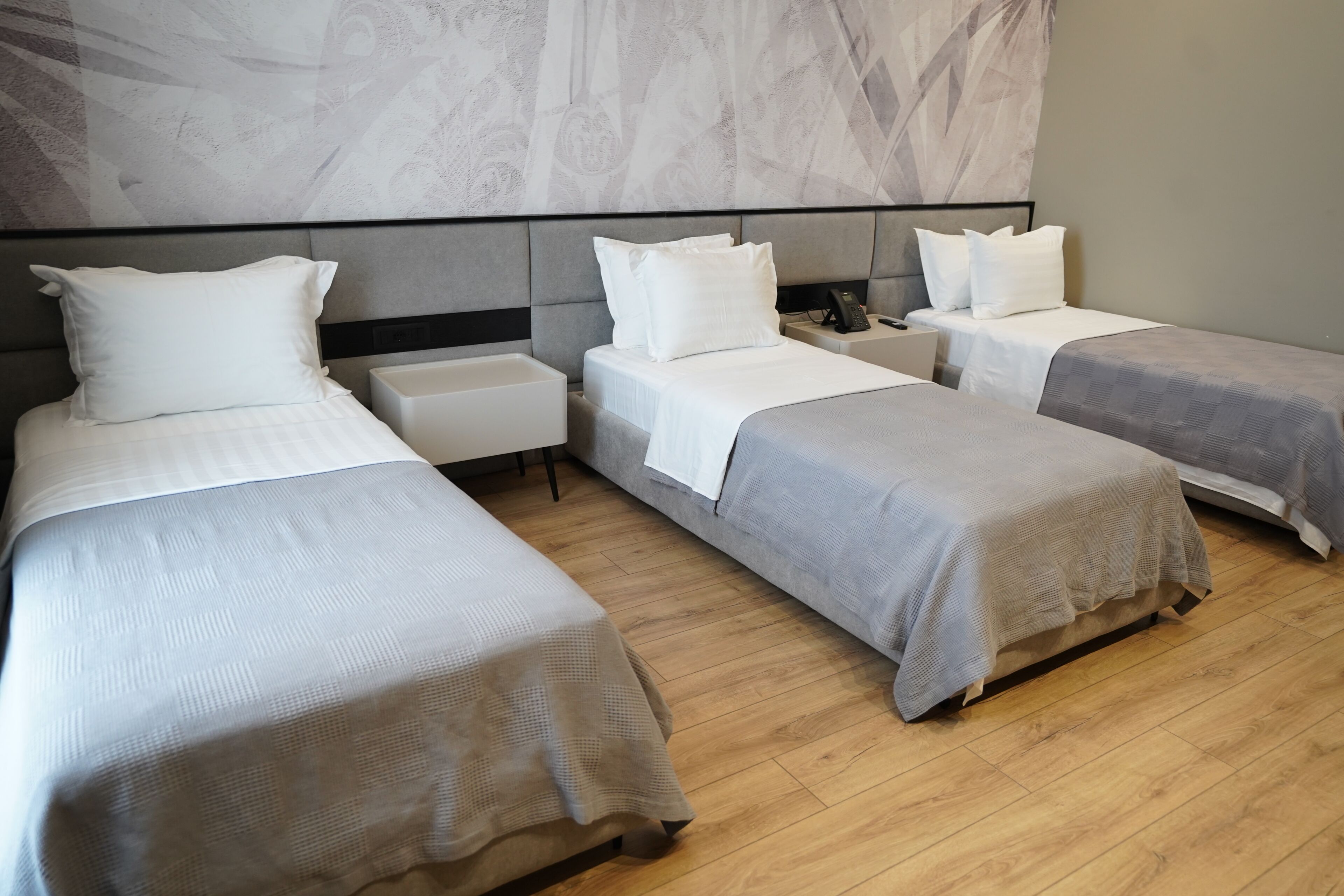 Habitación de hotel con tres camas individuales, una mesita de noche con teléfono y pared con diseño de mármol.