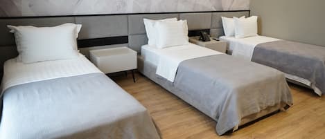 Une chambre d’hôtel avec trois lits simples, une table de chevet avec un téléphone et un mur décoré d’un motif imitant le marbre.